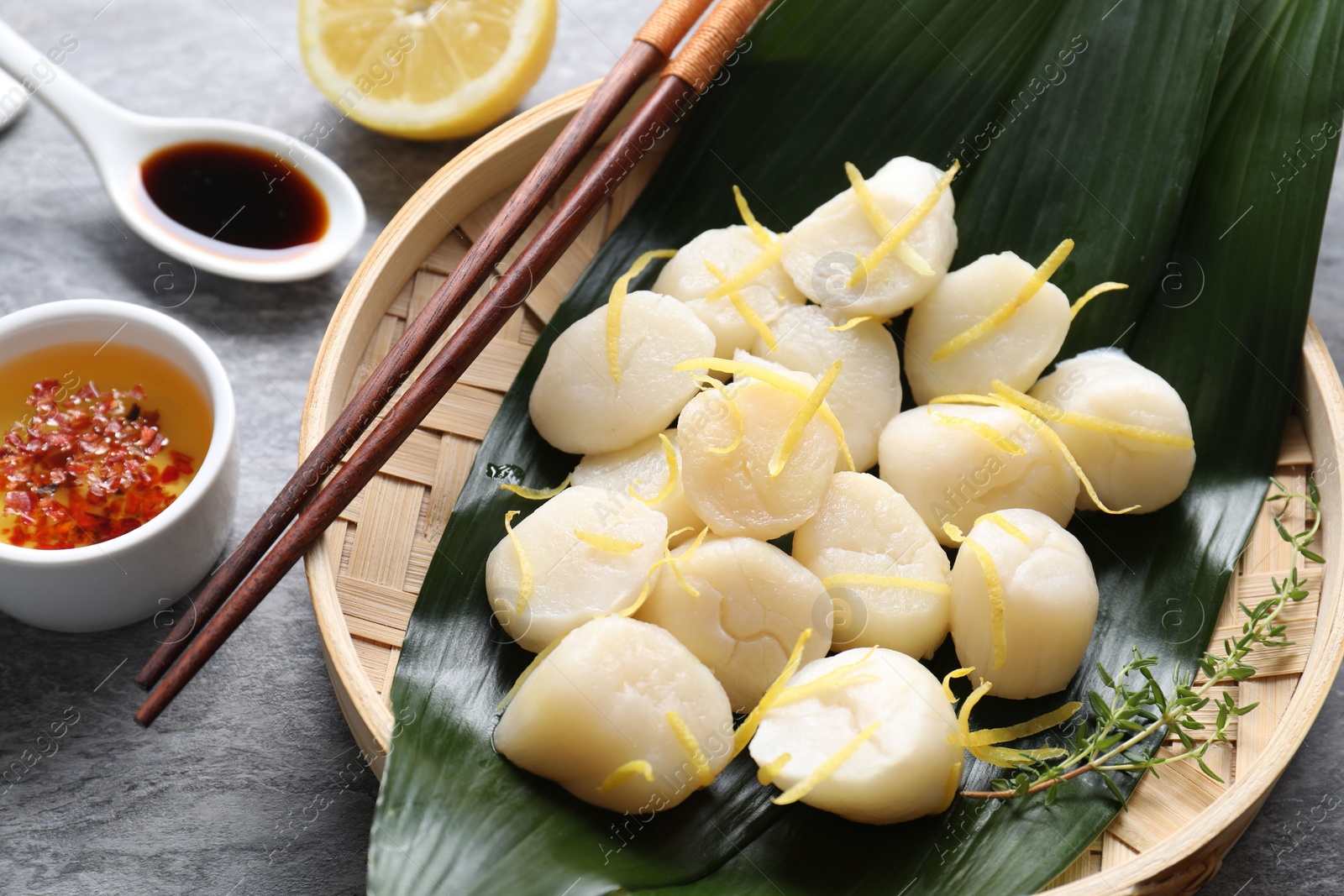 Photo of Raw scallops with thyme, lemon zest and sauces on grey marble table, closeup