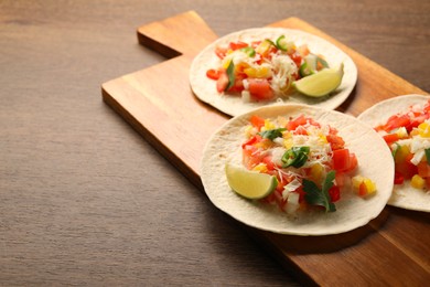 Photo of Delicious tacos with vegetables and lime on wooden table, closeup. Space for text