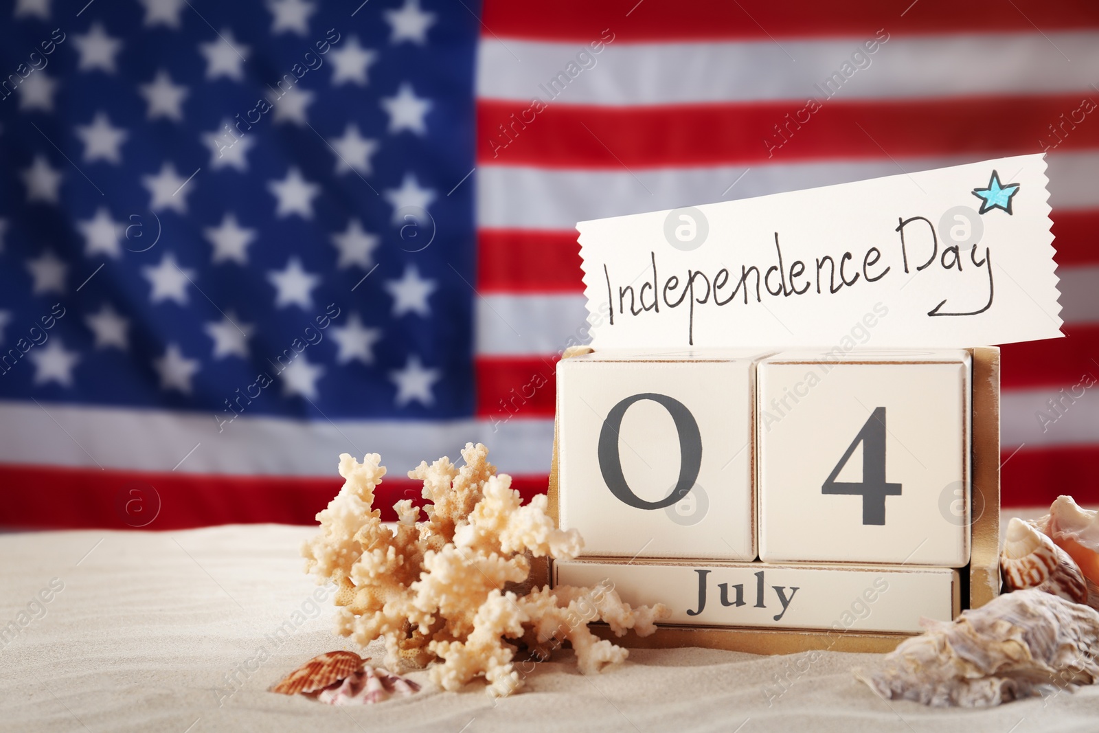 Photo of Composition with wooden calendar and card on sand against USA flag, space for text. Happy Independence Day