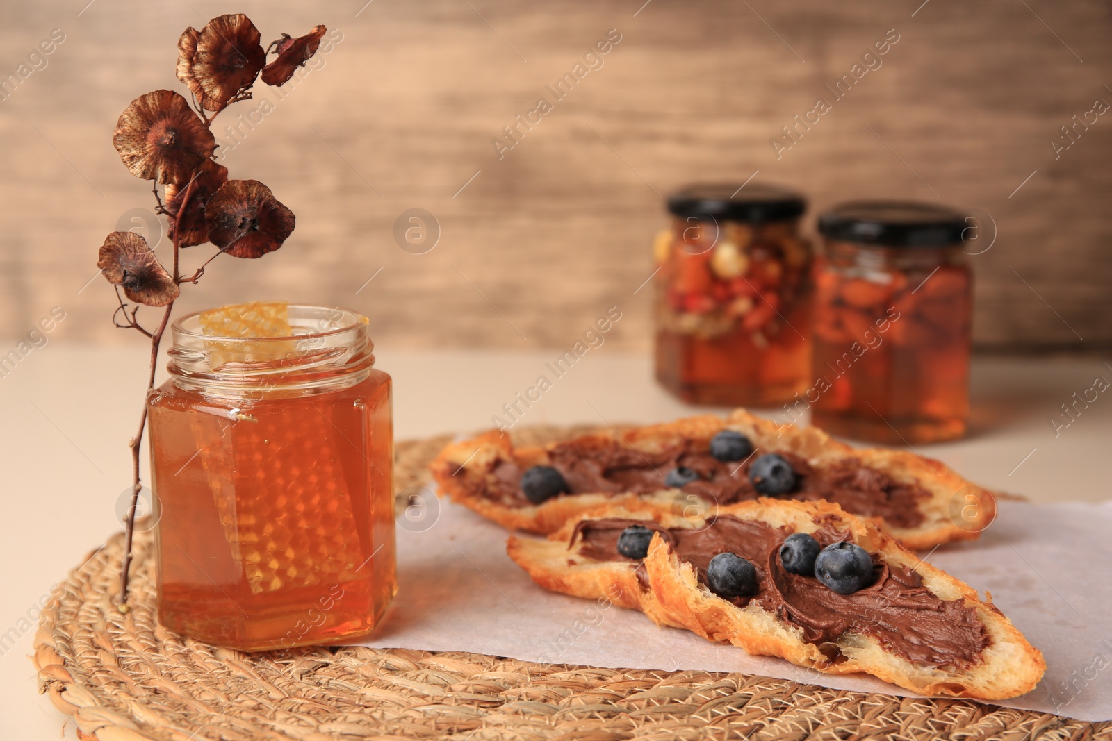 Photo of Composition with jar of honey and croissant on beige table