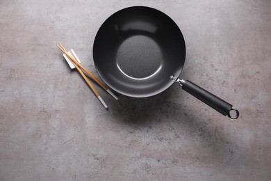 Empty iron wok and chopsticks on grey table, flat lay