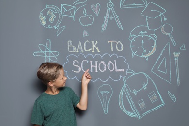 Little child near drawings and text BACK TO SCHOOL on grey background