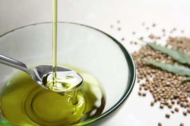 Pouring hemp oil into spoon over glass bowl, closeup