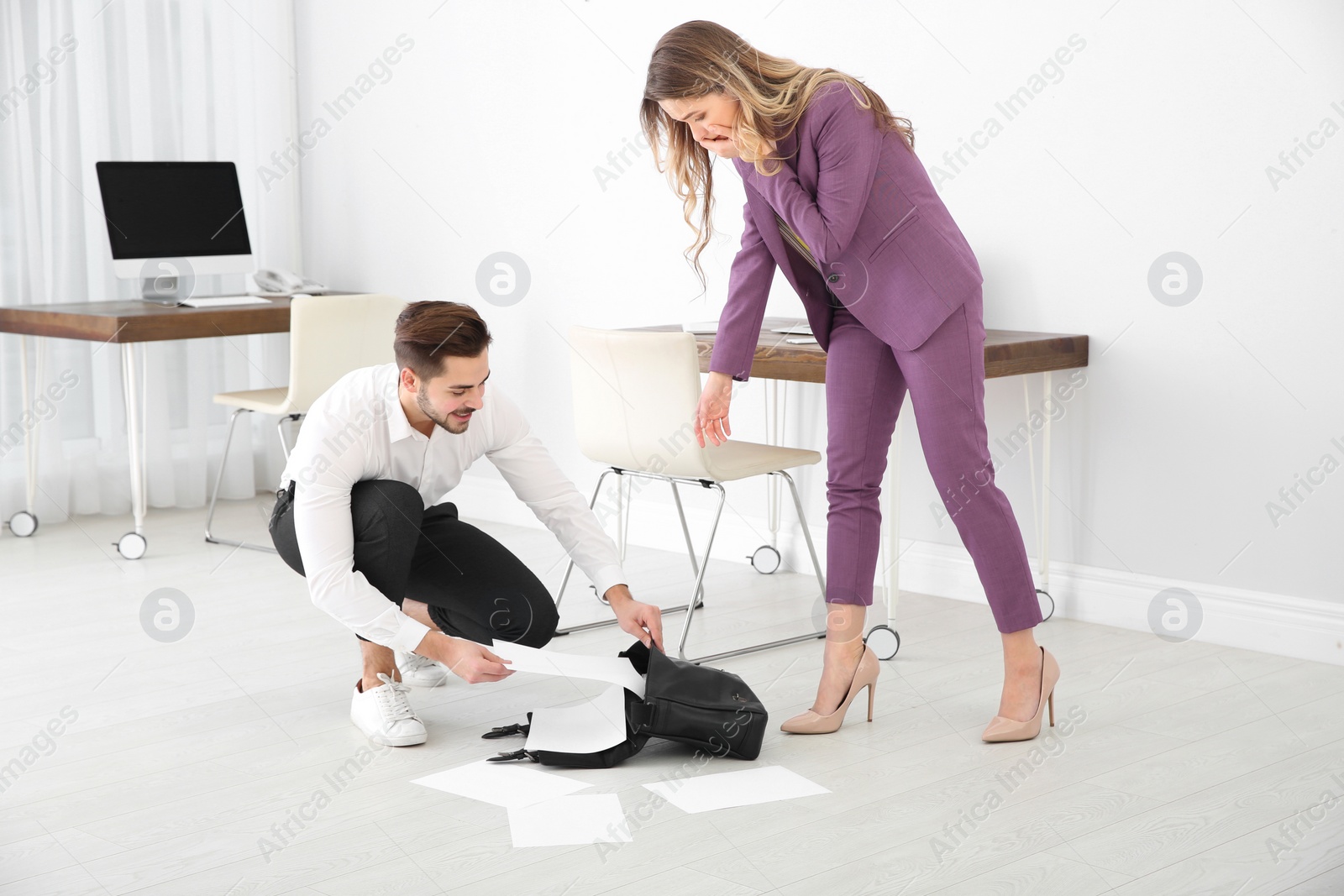 Photo of Young man helping his colleague to collect fallen documents in office