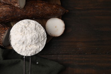 Photo of Scoop with cassava flour and roots on wooden table, flat lay. Space for text