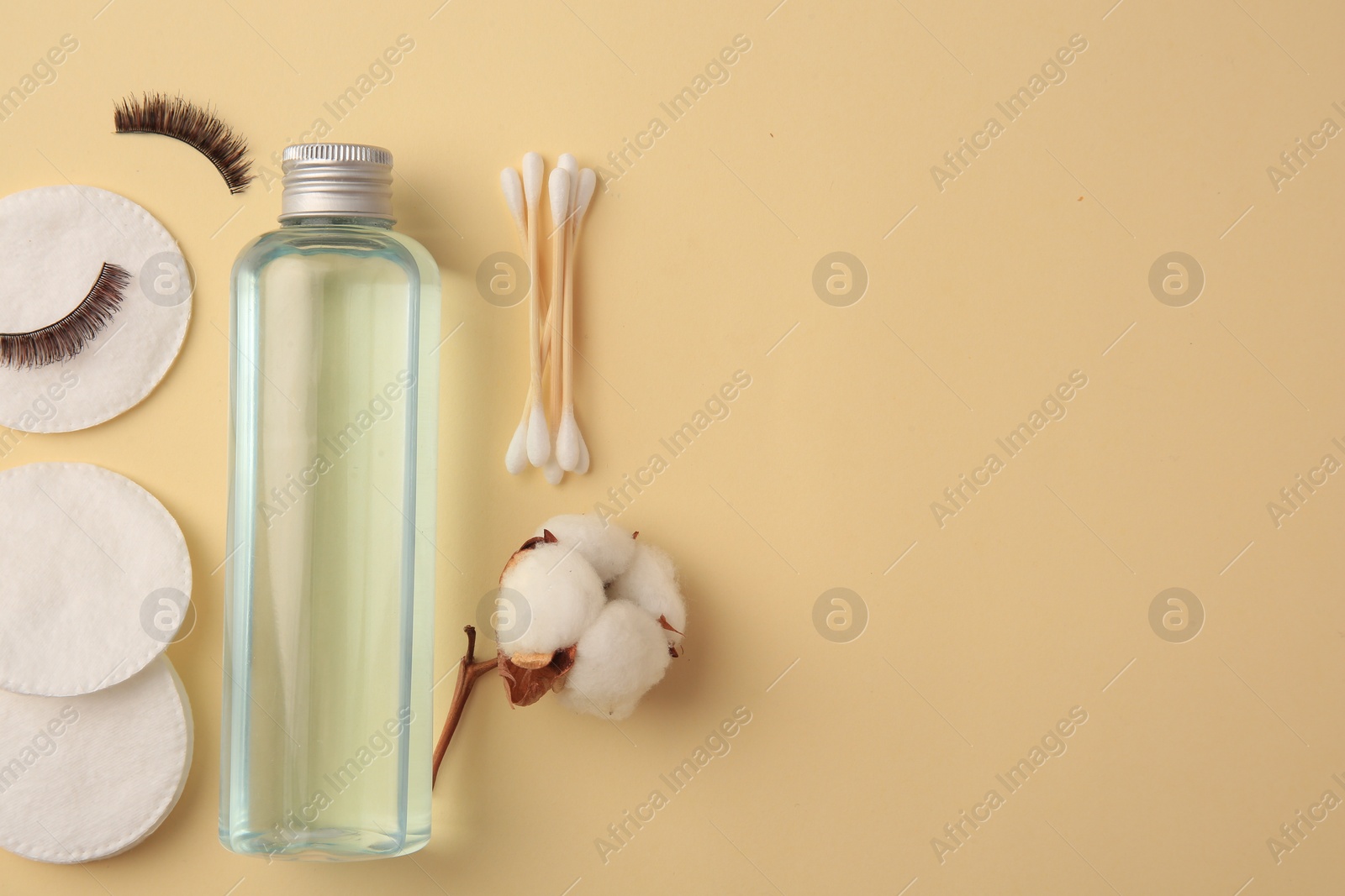 Photo of Bottle of makeup remover, cotton flower, pads, swabs and false eyelashes on yellow background, flat lay. Space for text