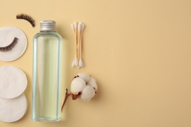 Bottle of makeup remover, cotton flower, pads, swabs and false eyelashes on yellow background, flat lay. Space for text