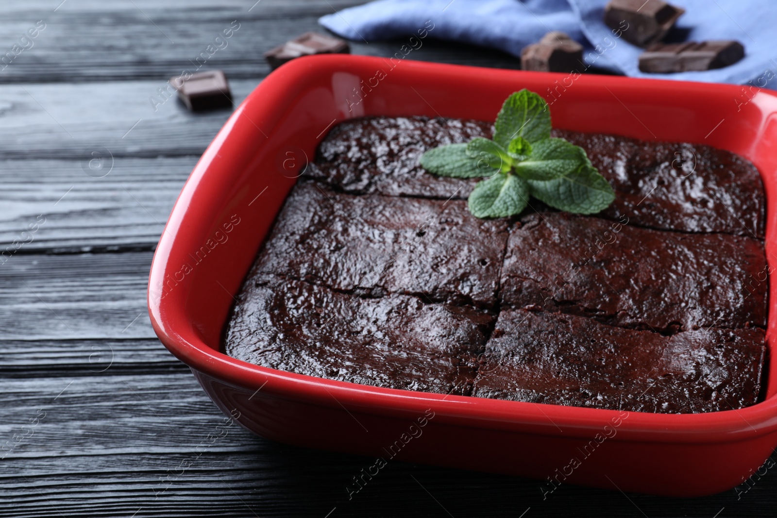 Photo of Delicious chocolate brownie with mint in baking dish on black wooden table, closeup