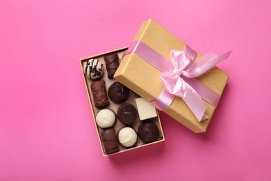 Photo of Open box with delicious chocolate candies on pink background, top view