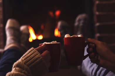 Couple with cups of delicious cocoa resting near fireplace at home, closeup. Winter vacation