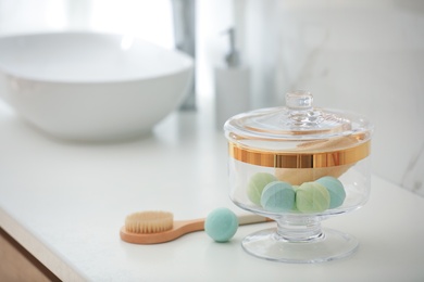 Jar with bath bombs and loofah sponge on white countertop in bathroom