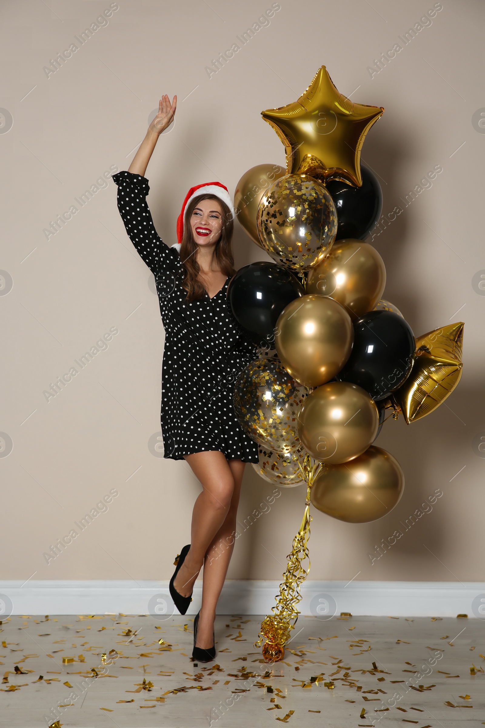 Photo of Happy woman in Santa hat with air balloons near beige wall indoors. Christmas party