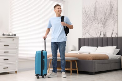 Photo of Smiling guest with suitcase and backpack exploring stylish hotel room