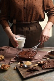 Photo of Woman with glass of milk and whisk mixing delicious chocolate cream at textured table, closeup
