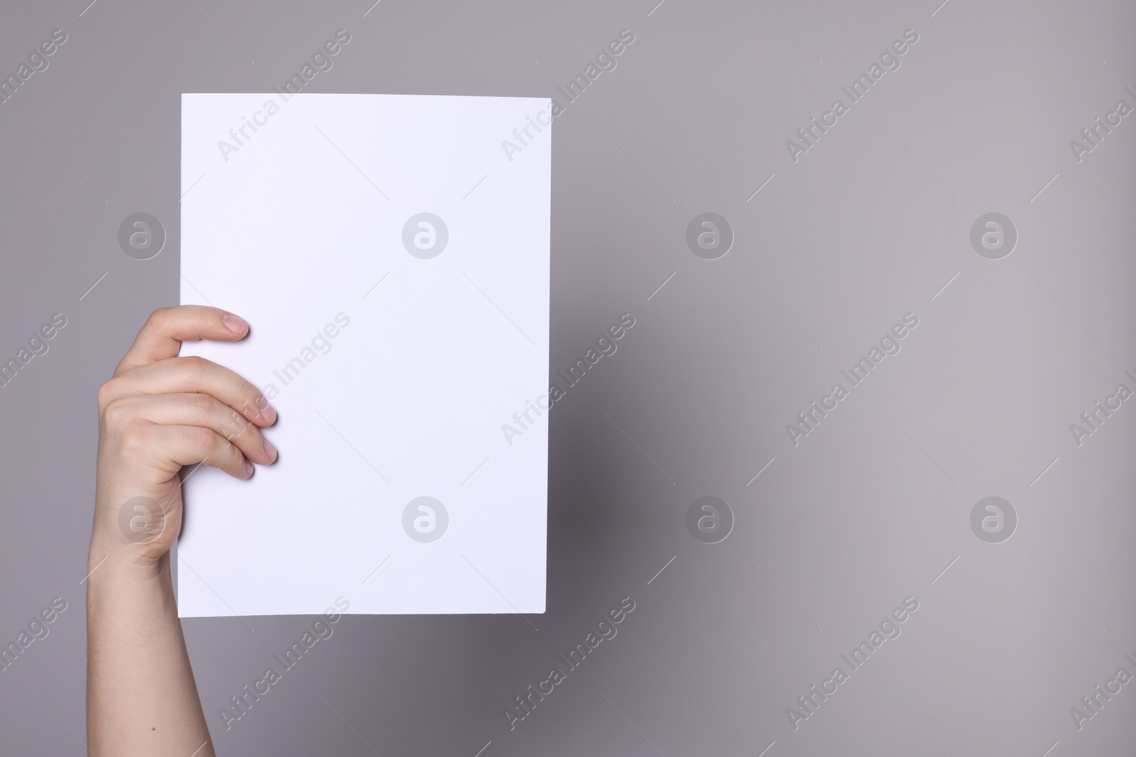 Photo of Woman holding sheet of paper on grey background, closeup. Mockup for design