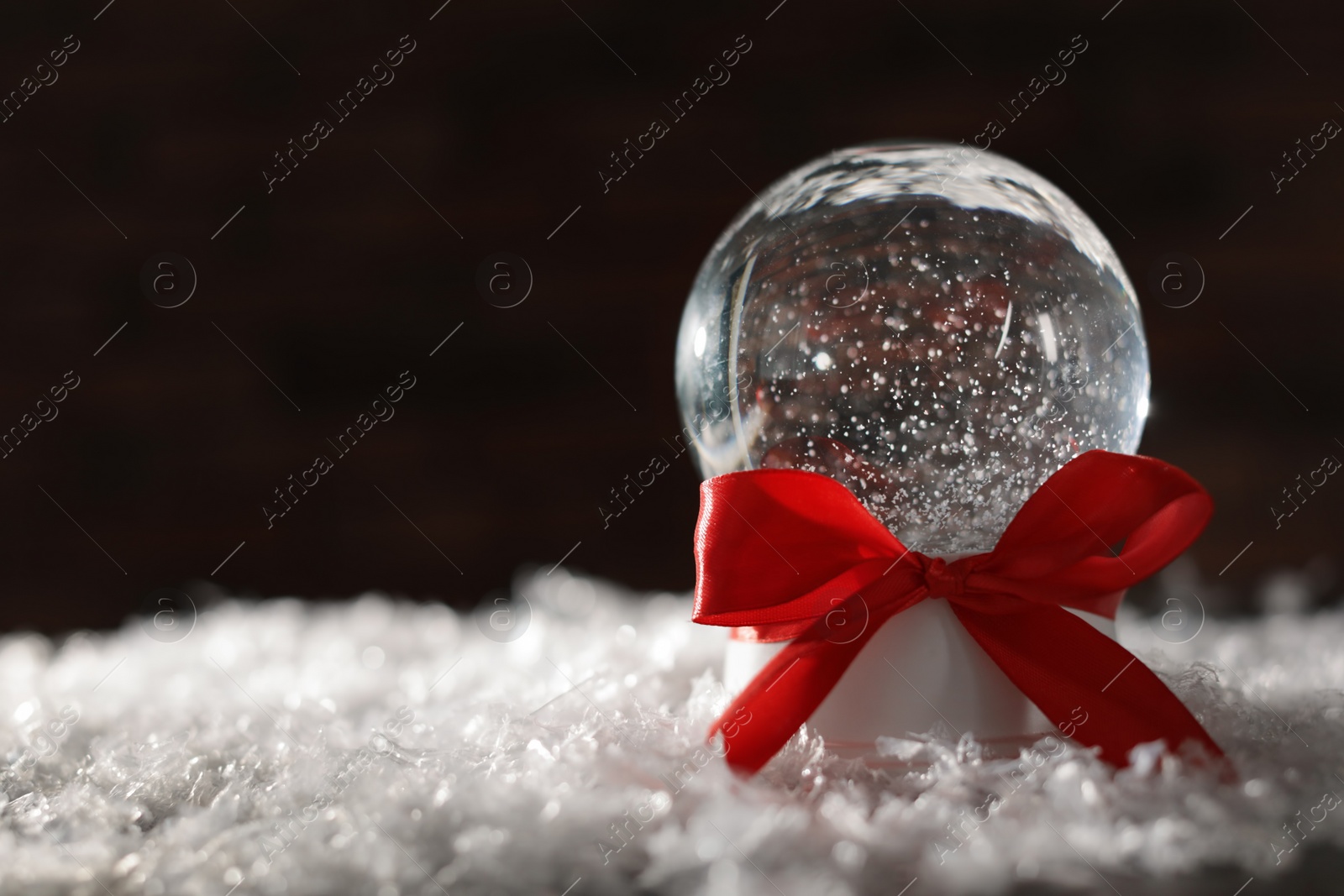 Photo of Christmas glass globe with artificial snow on blurred background. Space for text