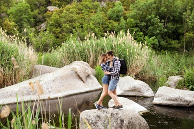 Photo of Cute young couple hugging on stone in middle of river. Camping season