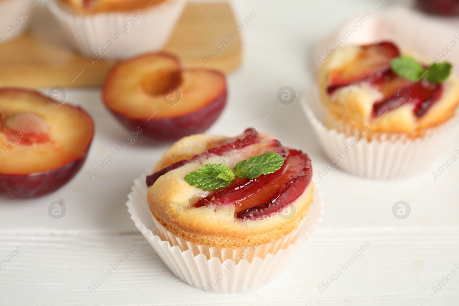 Photo of Delicious cupcakes with plums on white wooden table, closeup