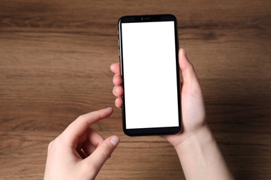 Woman holding smartphone with blank screen at wooden table, top view. Mockup for design