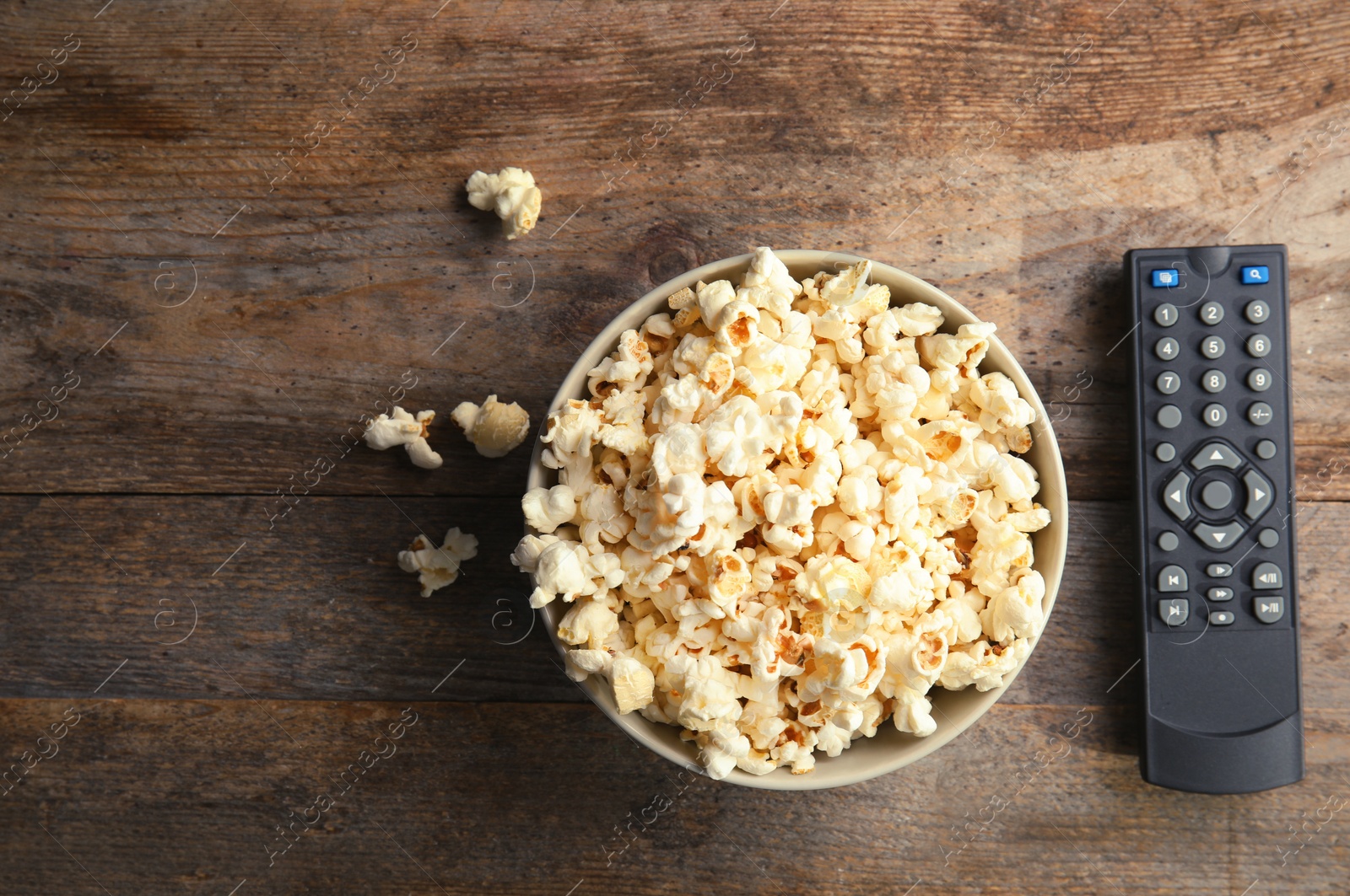 Photo of Bowl of popcorn and TV remote on wooden background, top view with space for text. Watching cinema