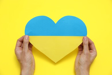 Photo of Man holding paper heart in colors of Ukrainian flag on yellow background, top view