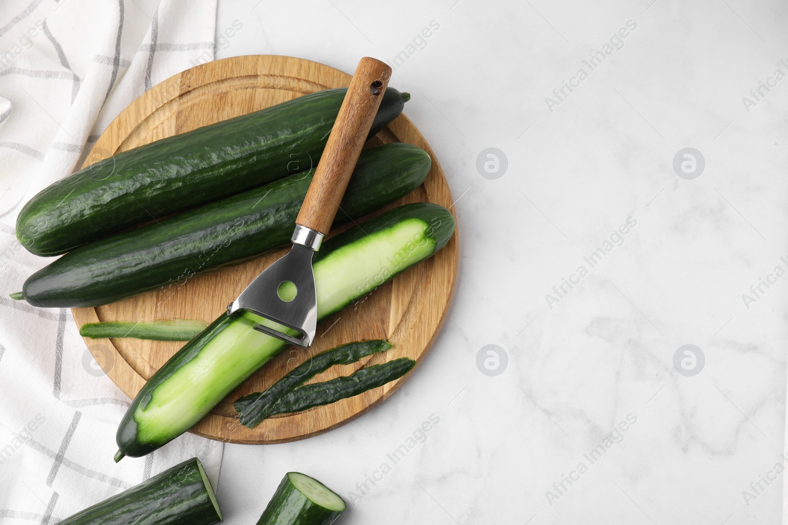 Photo of Fresh cucumbers and peeler on white marble table, top view. Space for text