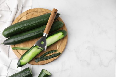 Fresh cucumbers and peeler on white marble table, top view. Space for text