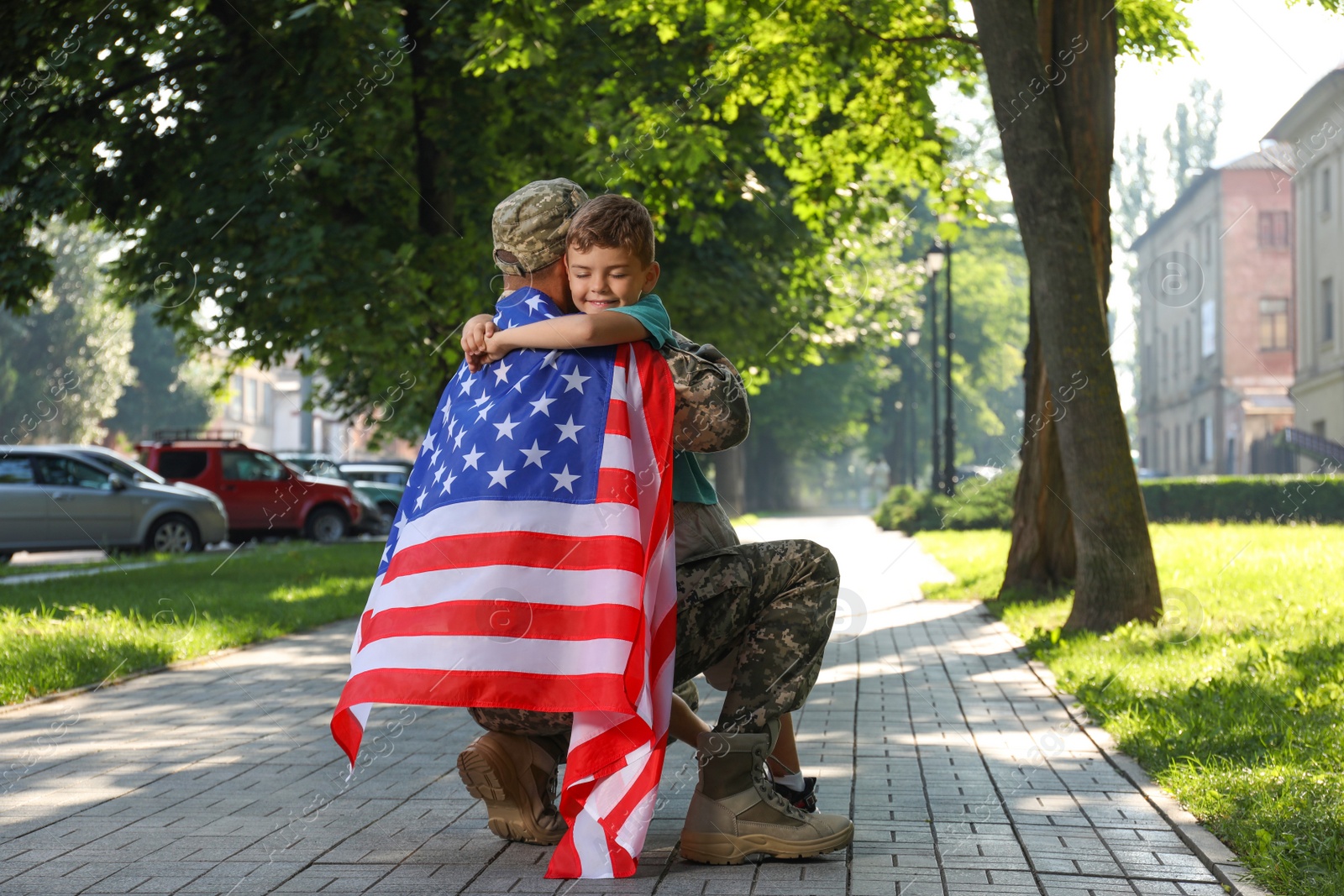 Photo of Soldier with flag of USA and his little son hugging outdoors