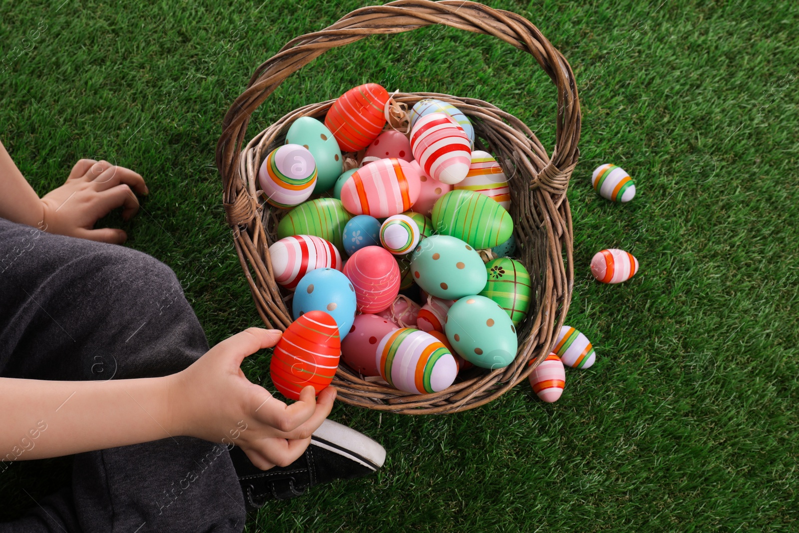 Photo of Little boy with basket full of dyed Easter eggs on green grass, closeup