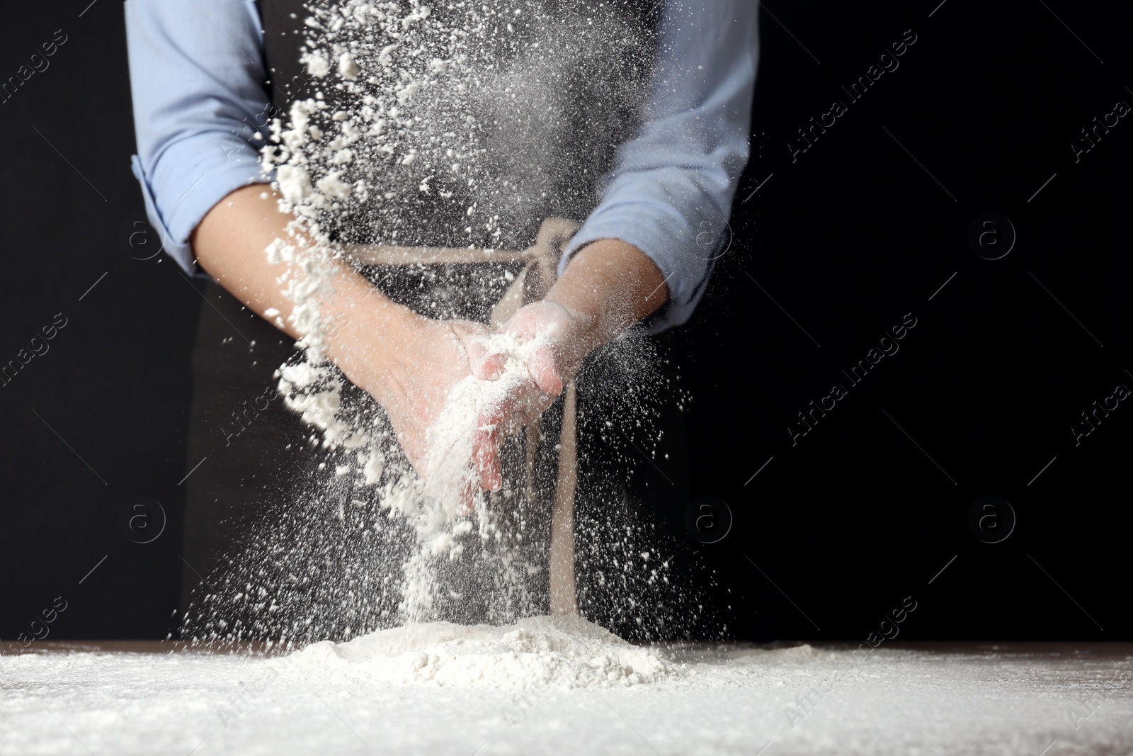 Photo of Woman working with flour at table against black background, closeup