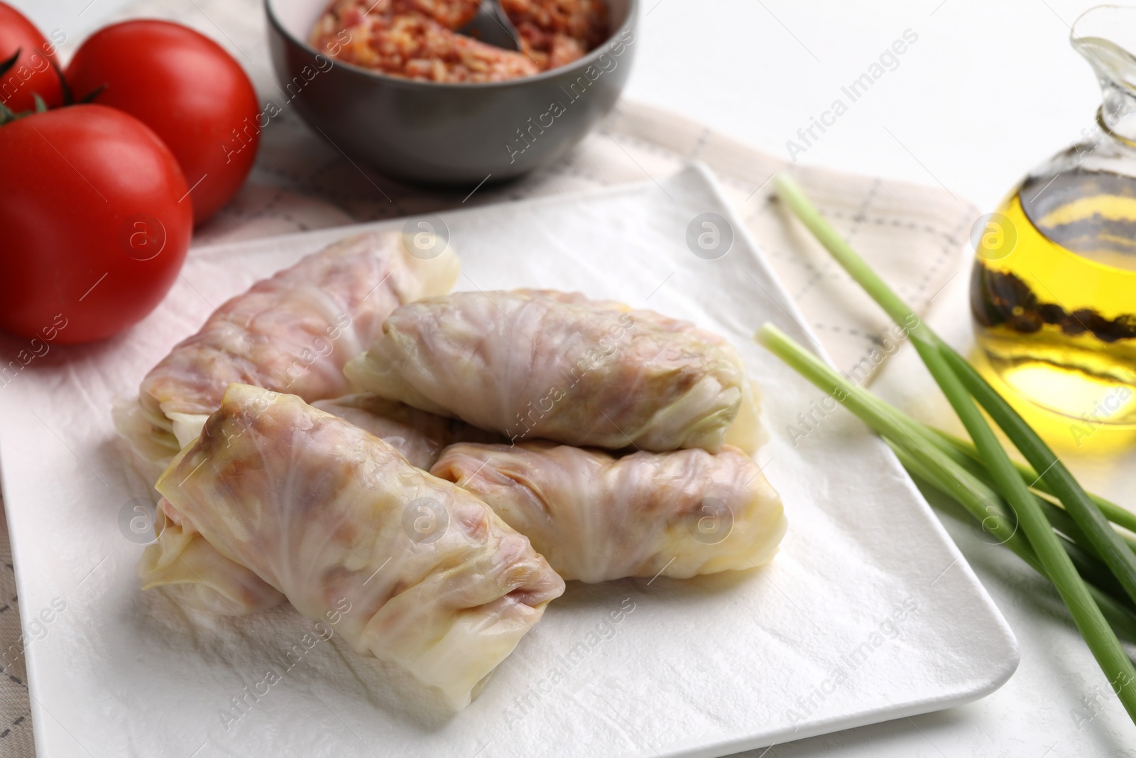 Photo of Uncooked stuffed cabbage rolls and ingredients on table, closeup