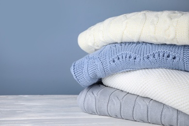 Stack of folded knitted sweaters on white wooden table against grey background, closeup. Space for text