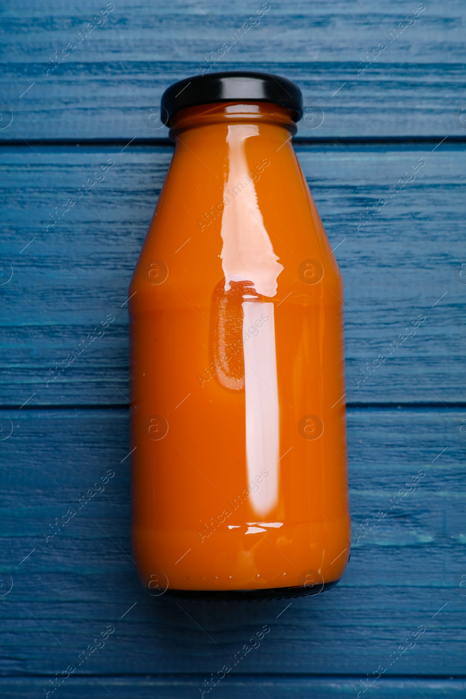 Photo of Healthy carrot juice in glass bottle on blue wooden table, top view