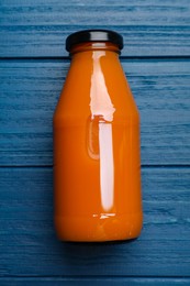 Photo of Healthy carrot juice in glass bottle on blue wooden table, top view