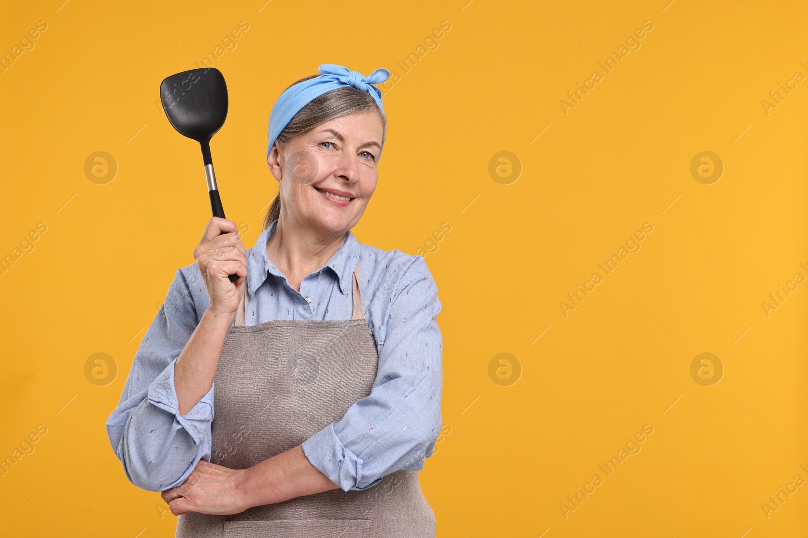 Photo of Happy housewife with turner on orange background, space for text