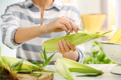 Woman husking corn at table, focus on hands