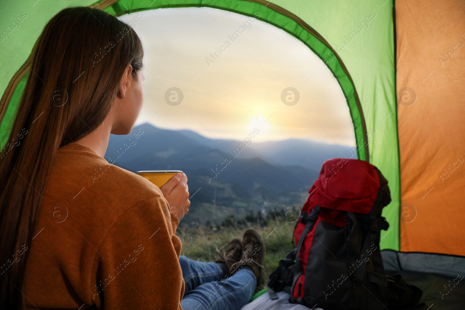 Photo of Young woman with drink inside of camping tent in mountains