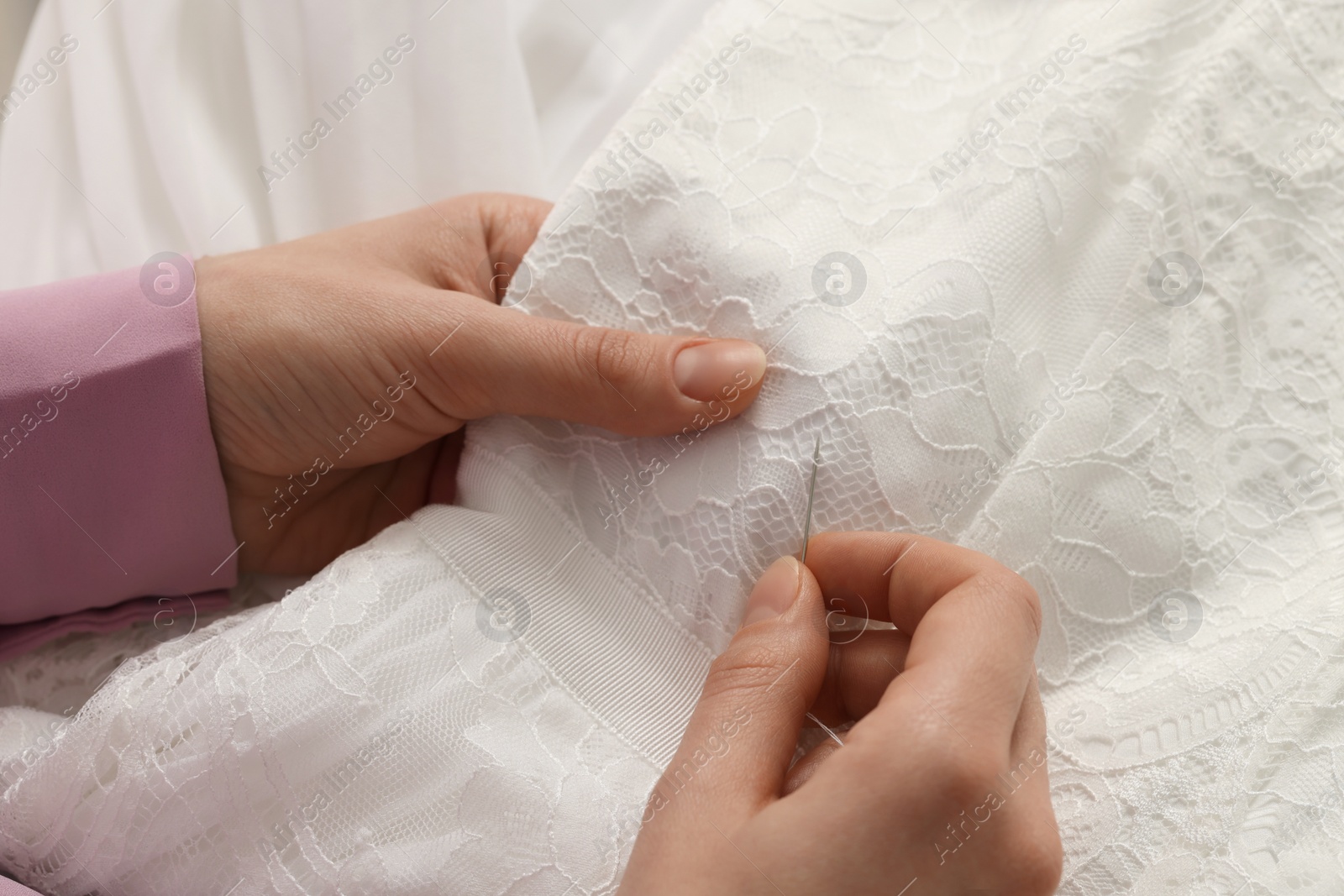 Photo of Dressmaker sewing wedding dress in atelier, closeup