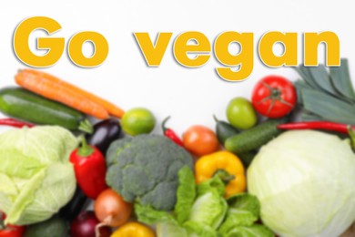 Image of Phrase Go Vegan and blurred view of fresh vegetables on white background, flat lay