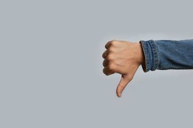 Man showing thumb down on grey background, closeup. Space for text