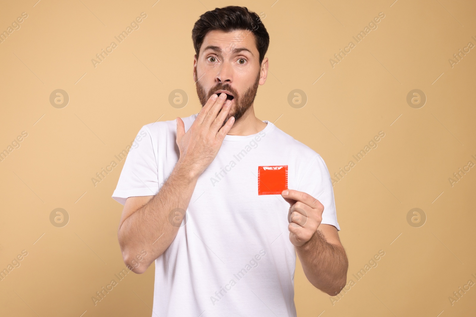 Photo of Emotional man holding condom on beige background. Safe sex