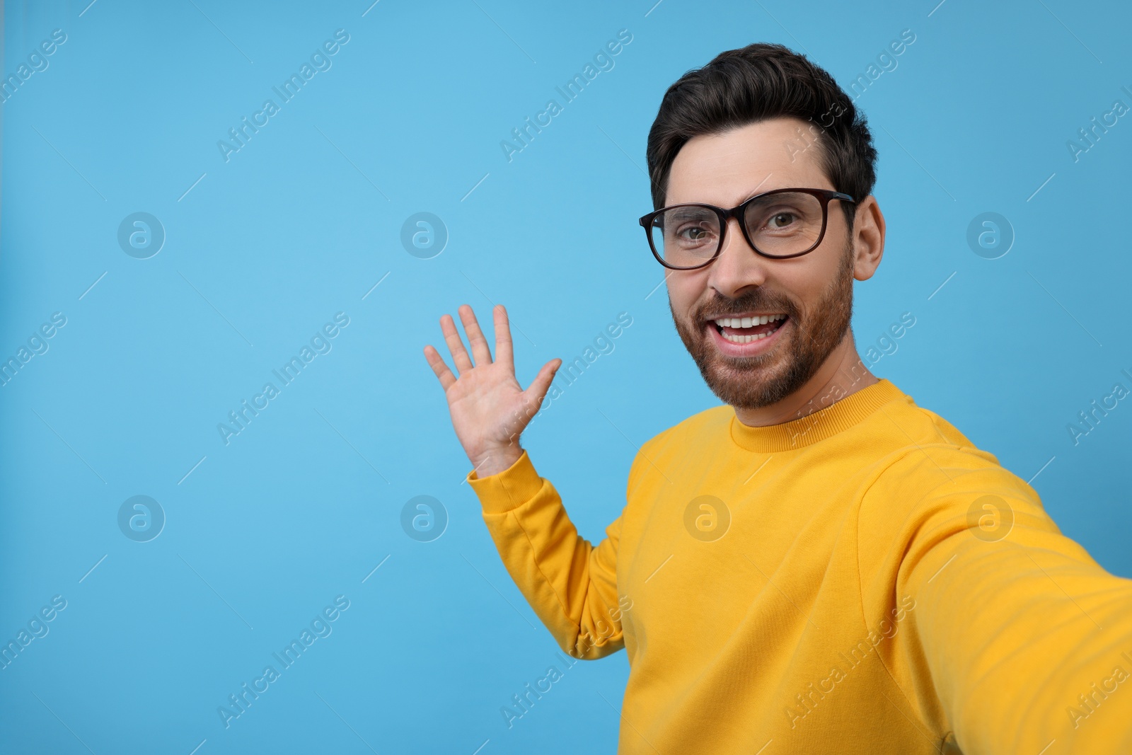 Photo of Smiling man taking selfie on light blue background, space for text