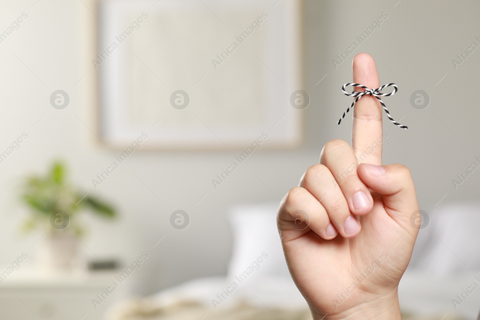 Photo of Man showing index finger with tied bow as reminder indoors, closeup. Space for text