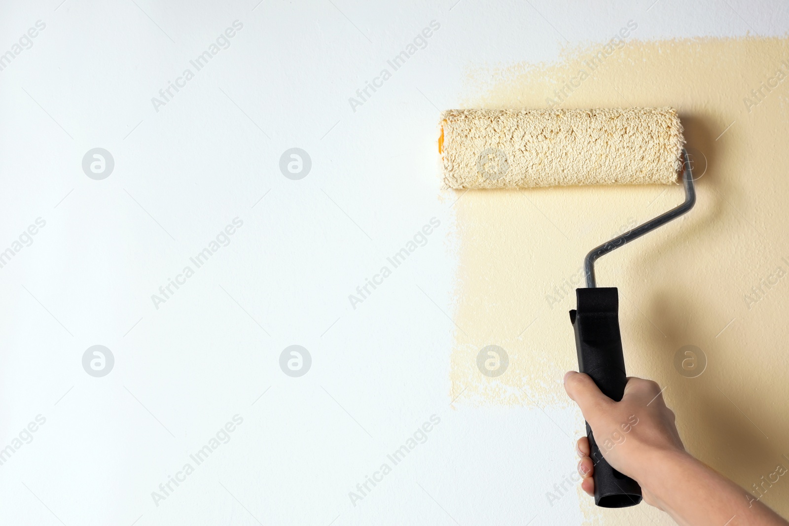 Photo of Woman painting white wall with beige dye, closeup. Space for text