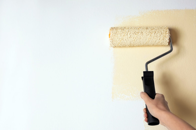 Photo of Woman painting white wall with beige dye, closeup. Space for text