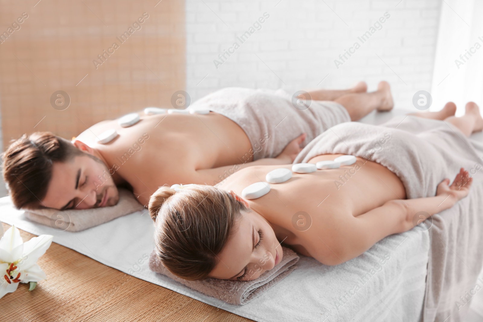 Photo of Romantic young couple receiving hot stone massage in spa salon