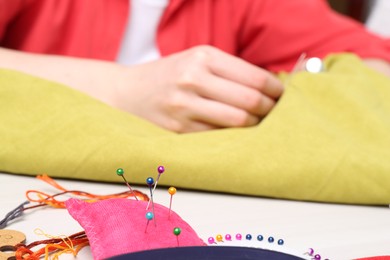 Photo of Woman with sewing thread embroidering on cloth at table, focus on pin cushion