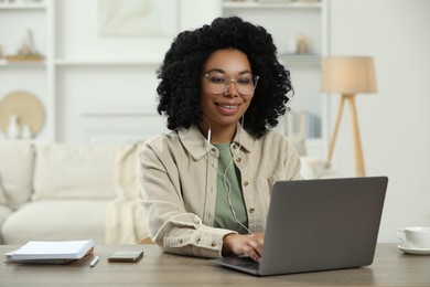 Photo of Happy young woman with earphones using laptop at wooden desk indoors