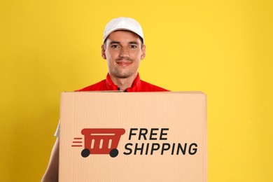Image of Happy young courier with cardboard box on yellow background. Free shipping