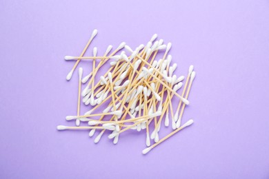 Wooden cotton buds on violet background, flat lay